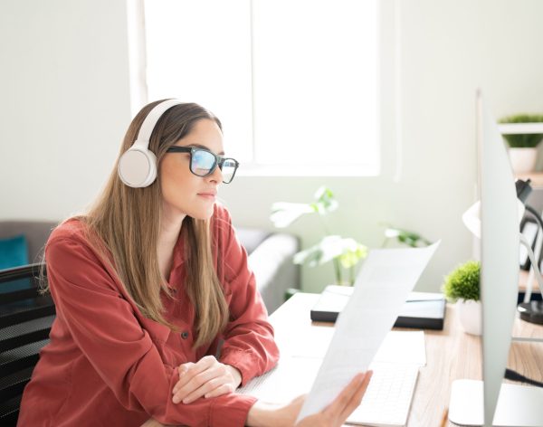 Pretty Caucasian brunette reading some documents and writing content while listening to music with headphones
