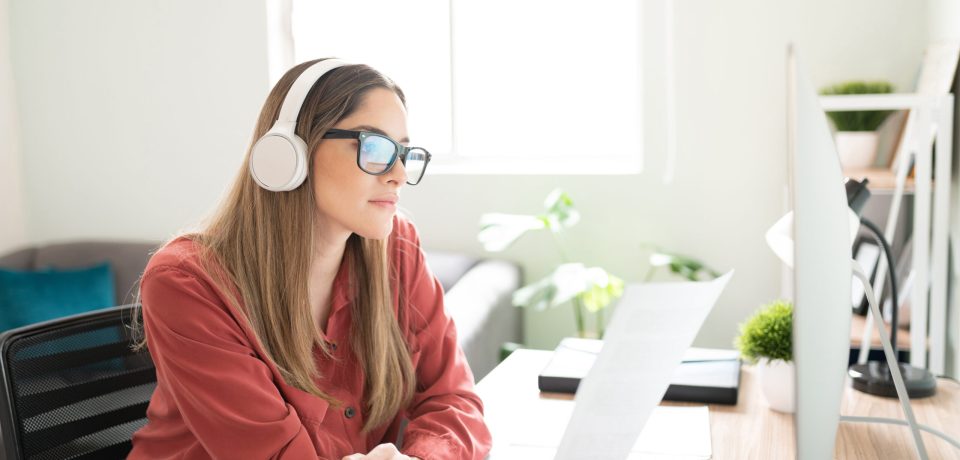 Pretty Caucasian brunette reading some documents and writing content while listening to music with headphones